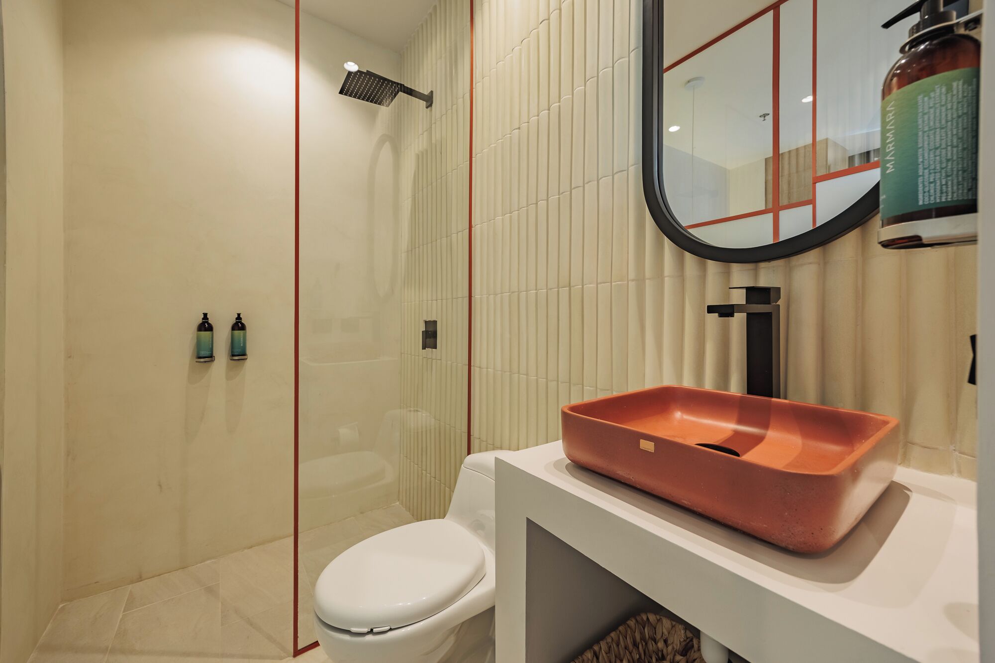 Une salle de bain moderne avec des toilettes blanches, une douche équipée d’un pommeau de douche à main et un lavabo avec un receveur rouge.