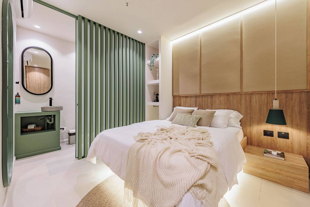 A modern bedroom with a large bed, a bedside table, a mirror, and a green sliding door.
