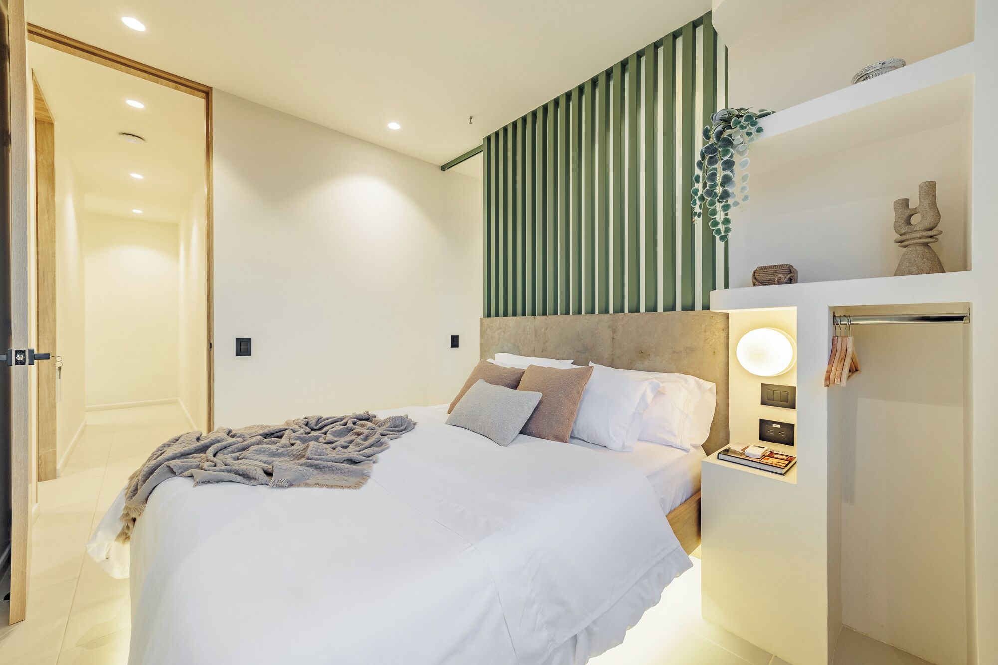 Une chambre moderne avec un grand lit, une table de chevet avec une lampe et une étagère murale agrémentée d’objets décoratifs.