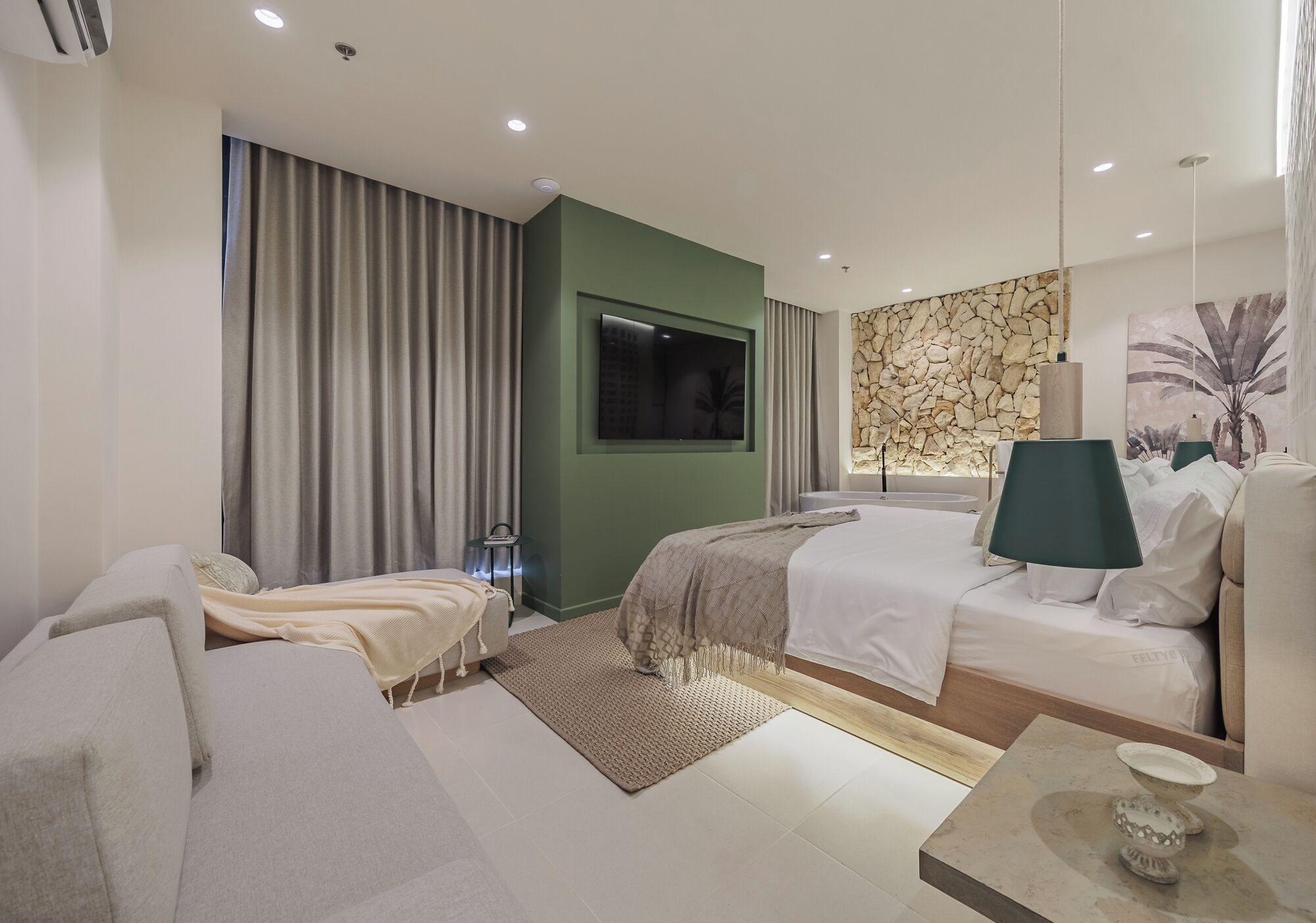 Una camera d'albergo moderna con un letto, un divano, una TV e una parete in pietra.