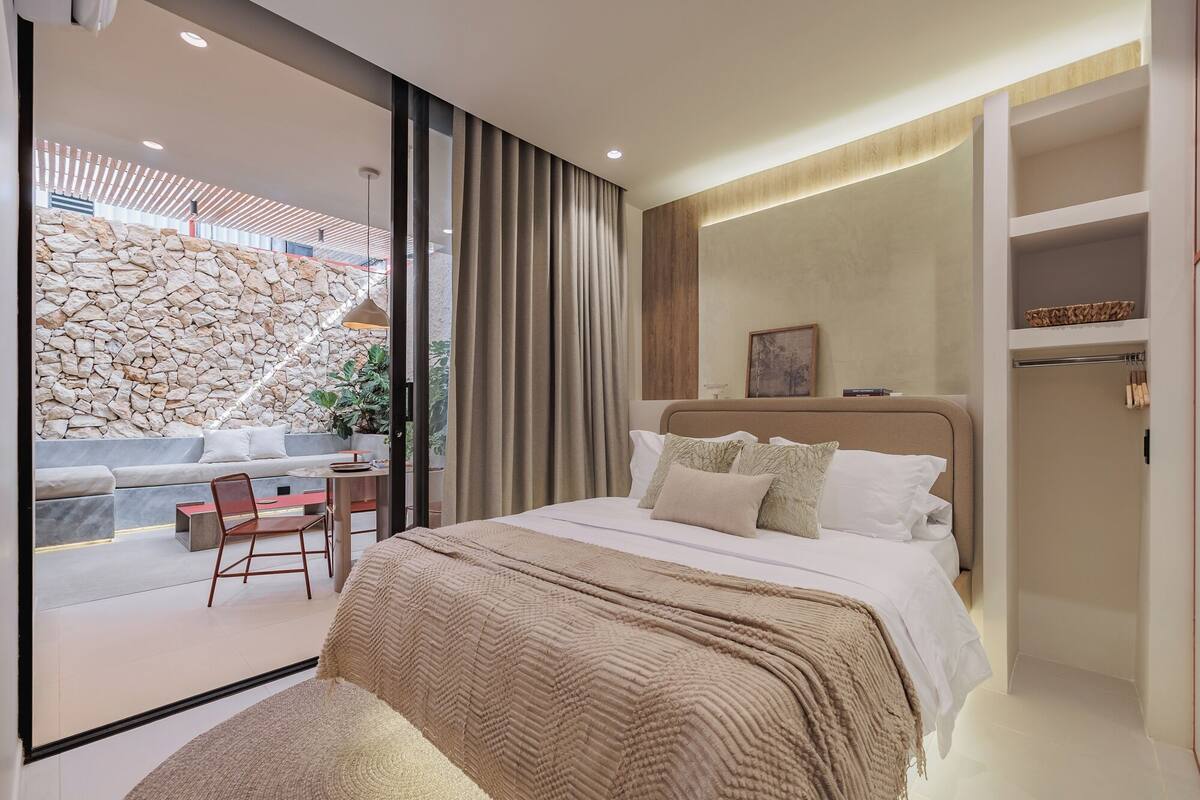 A modern bedroom with a large bed, a seating area with a table, and a stone wall.