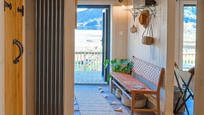 A wooden interior with a bench, a radiator, and a view of a snowy landscape through an open door.