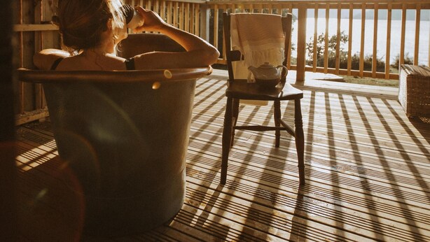 A wooden deck with a view of the water, a chair, and a bathtub.