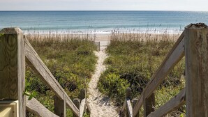 Un sentier en bois mène à une plage, et de chaque côté se trouve une clôture en bois.