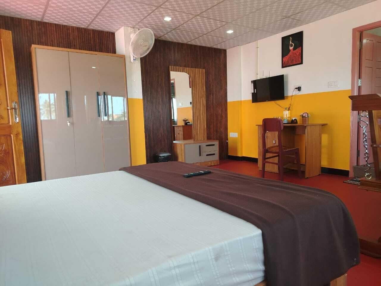 A hotel room with a bed, a desk, a chair, a wardrobe, and a television.