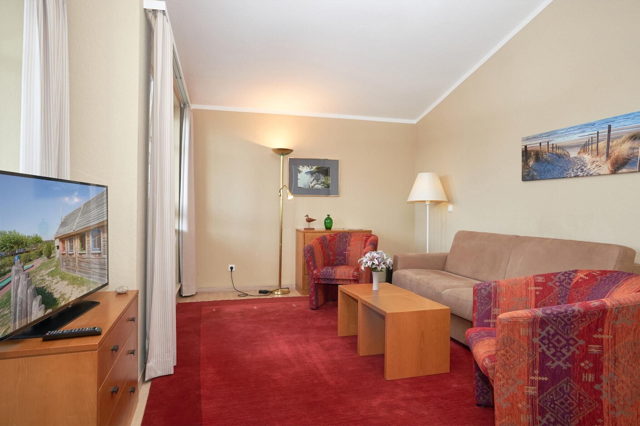 Een woonkamer met een televisie, bank, fauteuil en een salontafel met een vaas.