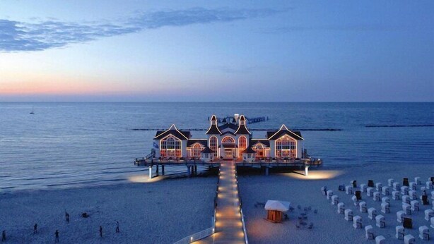 A beachfront hotel with a central building and a pier extending into the sea.
