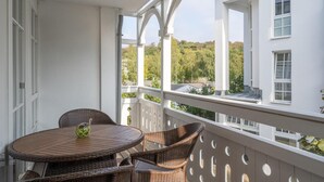 A balcony with wicker furniture and a view of a white building and trees.