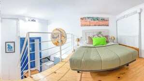 Une chambre à coucher avec un lit à la forme arrondie, un escalier et un tableau représentant une scène de plage.