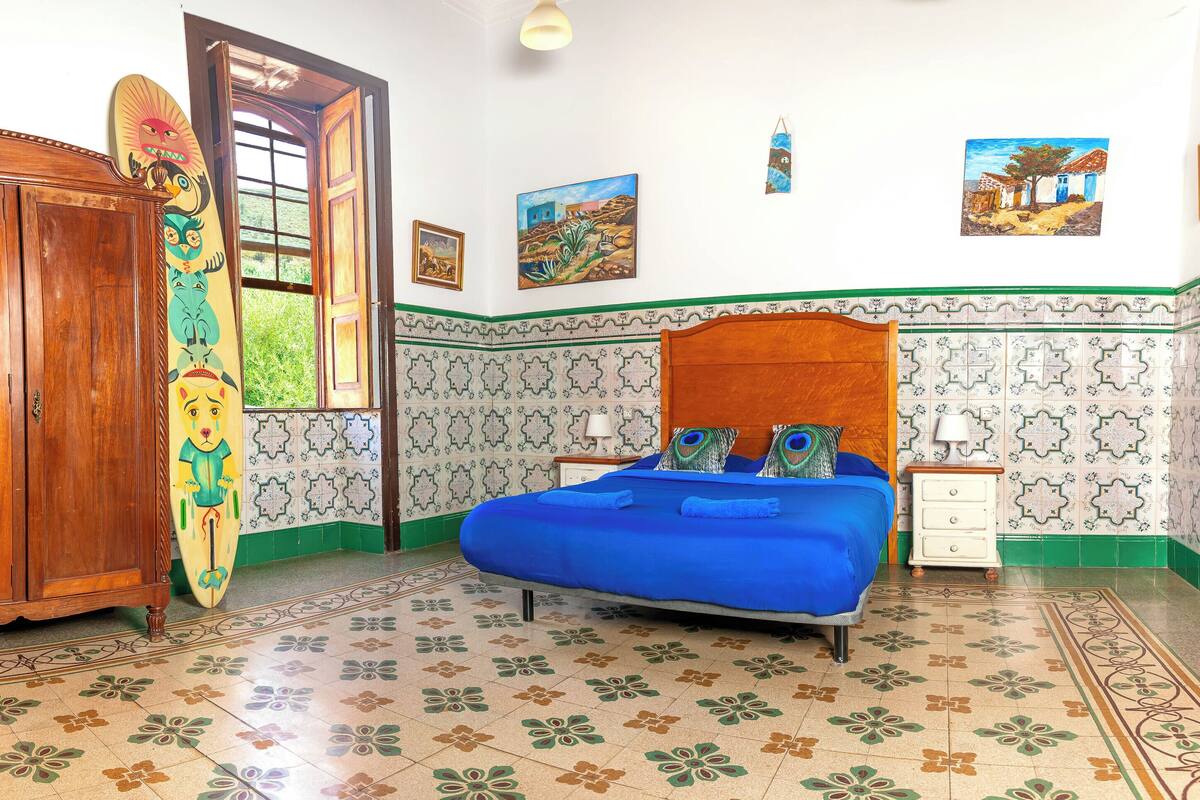Quarto com guarda-roupa de madeira, cama com roupa de cama azul e paredes e chão estampados.