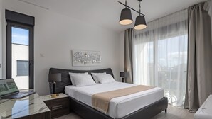 Et moderne hotelværelse med seng, skrivebord med computer, sengetøj og et stort vindue med gardiner.