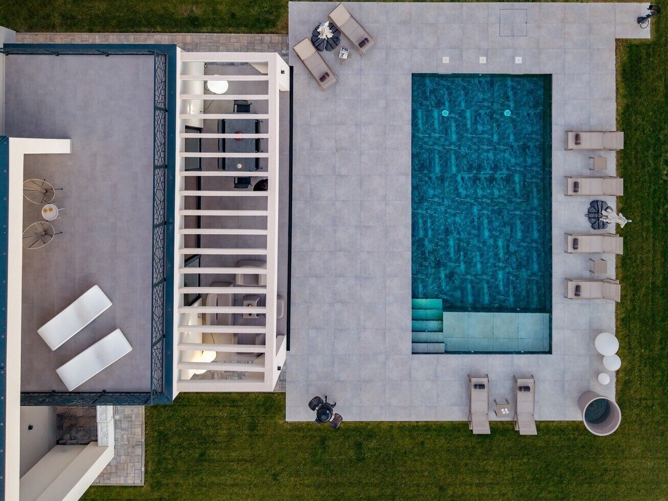 Vista aerea di una moderna area piscina all'aperto con una vasca rettangolare, lettini, un'area relax e un portico coperto.