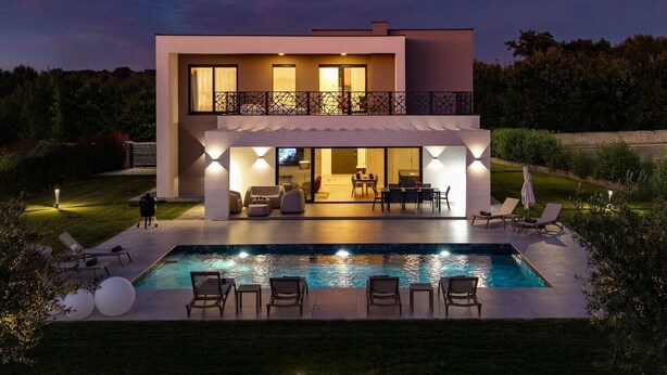Et moderne hus i to etager med swimmingpool, udendørs siddepladser og en balkon.