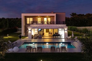 Una moderna casa a due piani con piscina, area salotto esterna e un balcone.
