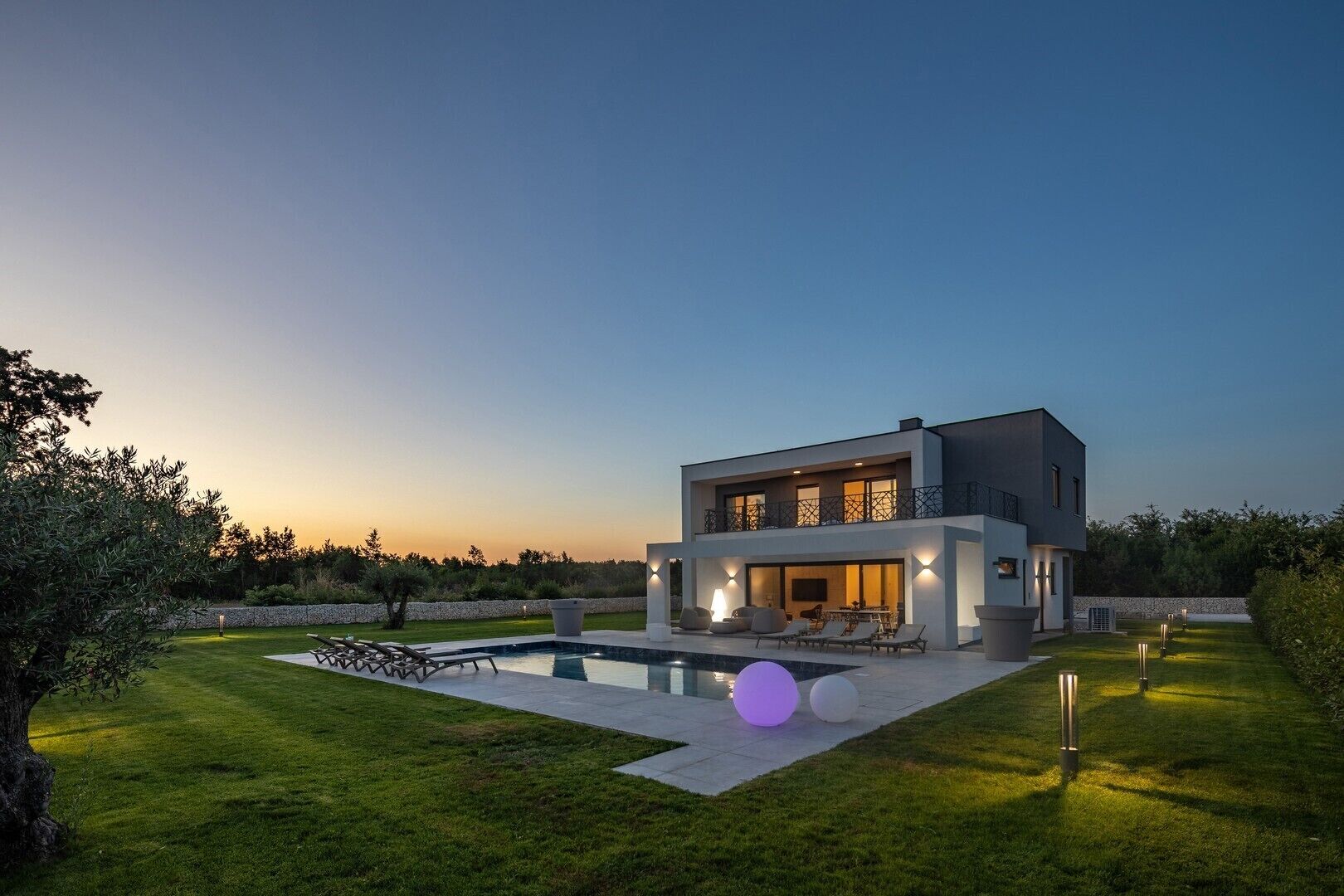 Una casa moderna de dos pisos con piscina, zona de estar exterior y césped cuidado.