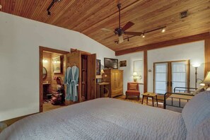 A bedroom with a large bed, wooden ceiling, a ceiling fan, a wardrobe, a desk, and a chair.