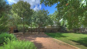 A fenced outdoor area with a dirt path, green grass, and trees.
