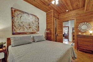 Un dormitorio con una cama grande, paredes de madera, un ventilador de techo, un cuadro, un aparador y un espejo.