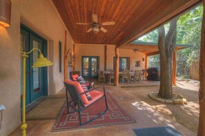 Un patio al aire libre con techo de madera, zona de comedor y un árbol grande.