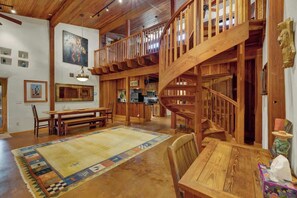 A spacious interior with a wooden staircase, a dining area with a bench, and a kitchen in the background. - The Willows-Award Winning New York Magazine Home! (Fredericksburg)