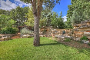 A stone wall with a rustic garden and a large tree in the foreground. - The Willows-Award Winning New York Magazine Home! (Fredericksburg)