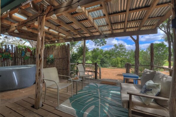 An outdoor patio with wooden furniture, a hot tub, and a view of the surrounding greenery.