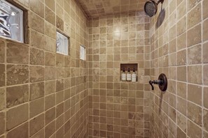 A tiled shower with a handheld showerhead and a small shelf with toiletries.