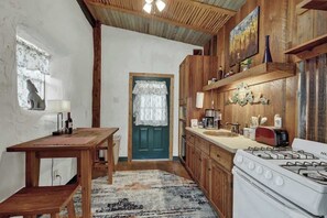 A rustic kitchen with wooden cabinets, a stove, a sink, and a dining table.