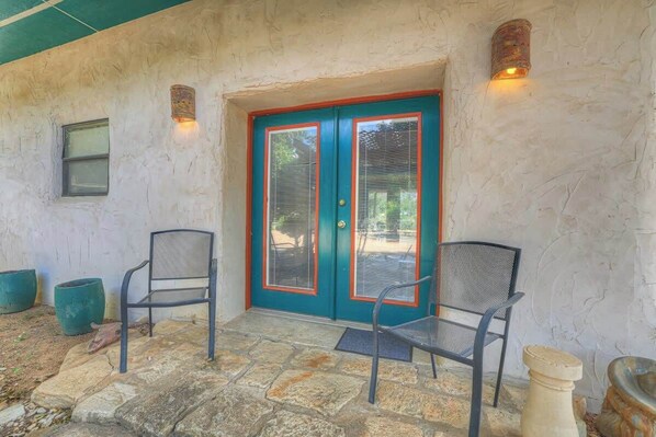 A stone patio with two chairs and a teal double door with red trim.