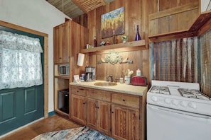 Una cocina con gabinetes de madera, estufa, fregadero y microondas.