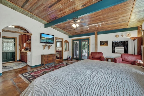 A spacious bedroom with a large bed, wooden ceiling, and a television mounted on the wall.