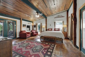 A spacious bedroom with a wooden ceiling, a large bed, a red leather chair, and a patterned rug.