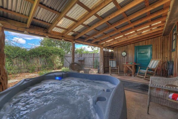 A hot tub under a wooden pergola with a rustic wooden fence and a green door in the background.