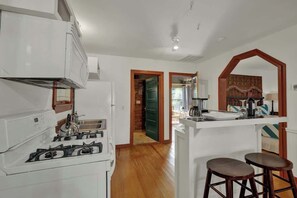 Una cocina con estufa a gas, piso de madera y una pequeña barra con taburetes.