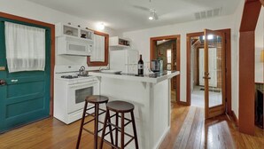 A kitchen with a central island, white cabinets, a stove, and two stools.