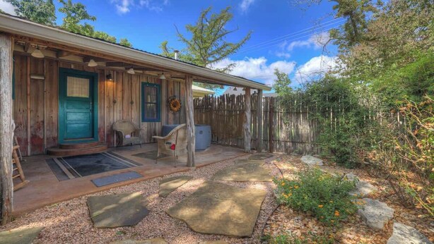 A rustic cabin with a wooden exterior, a green door, and a porch with a chair and a small table.