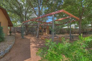 Área de varanda externa com pérgola, assentos e um pequeno jardim.