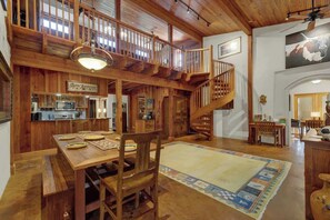 Un comedor amplio con una mesa y sillas de madera, una escalera y una cocina al fondo.