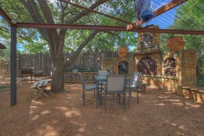Un patio al aire libre con una chimenea de piedra rústica, una mesa de madera y sillas de metal.