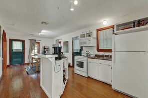 Una cocina compacta con electrodomésticos blancos, un comedor con mesa y sillas, y piso de madera.