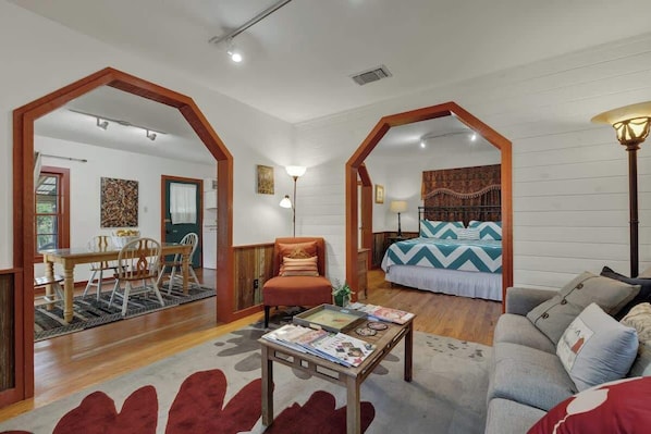 A spacious living area with a dining table, a sofa, a bed with patterned bedding, and a coffee table with magazines.