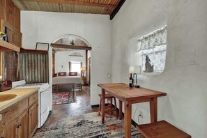 Una cocina compacta con armarios de madera, una mesa de comedor y una ventana con cortina.