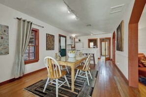 Un salón espacioso con una mesa de comedor de madera, sillas blancas y un tapete estampado.