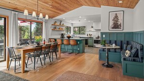 Une cuisine moderne avec un plafond en bois, un coin repas avec une table et des chaises en bois, et un espace détente avec un canapé et une petite table.