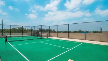 An outdoor tennis court with a green surface and a net, surrounded by a chain-link fence.