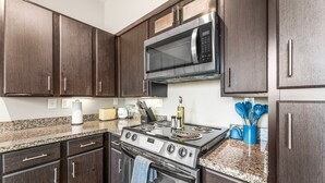 A kitchen with dark wood cabinets, stainless steel appliances, granite countertops, and a built-in microwave. - Fun Soco 1BR King Suite w Gympickleballlaundry (Austin)