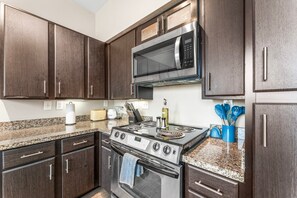 A kitchen with dark wood cabinets, stainless steel appliances, granite countertops, and a built-in microwave. - Fun Soco 1BR King Suite w Gympickleballlaundry (Austin)