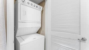 Ein kleiner Hauswirtschaftsraum mit einer gestapelten Waschmaschine und einem Trockner, einer Tür mit Lamellen und einem sichtbaren Thermostat am Trockner.