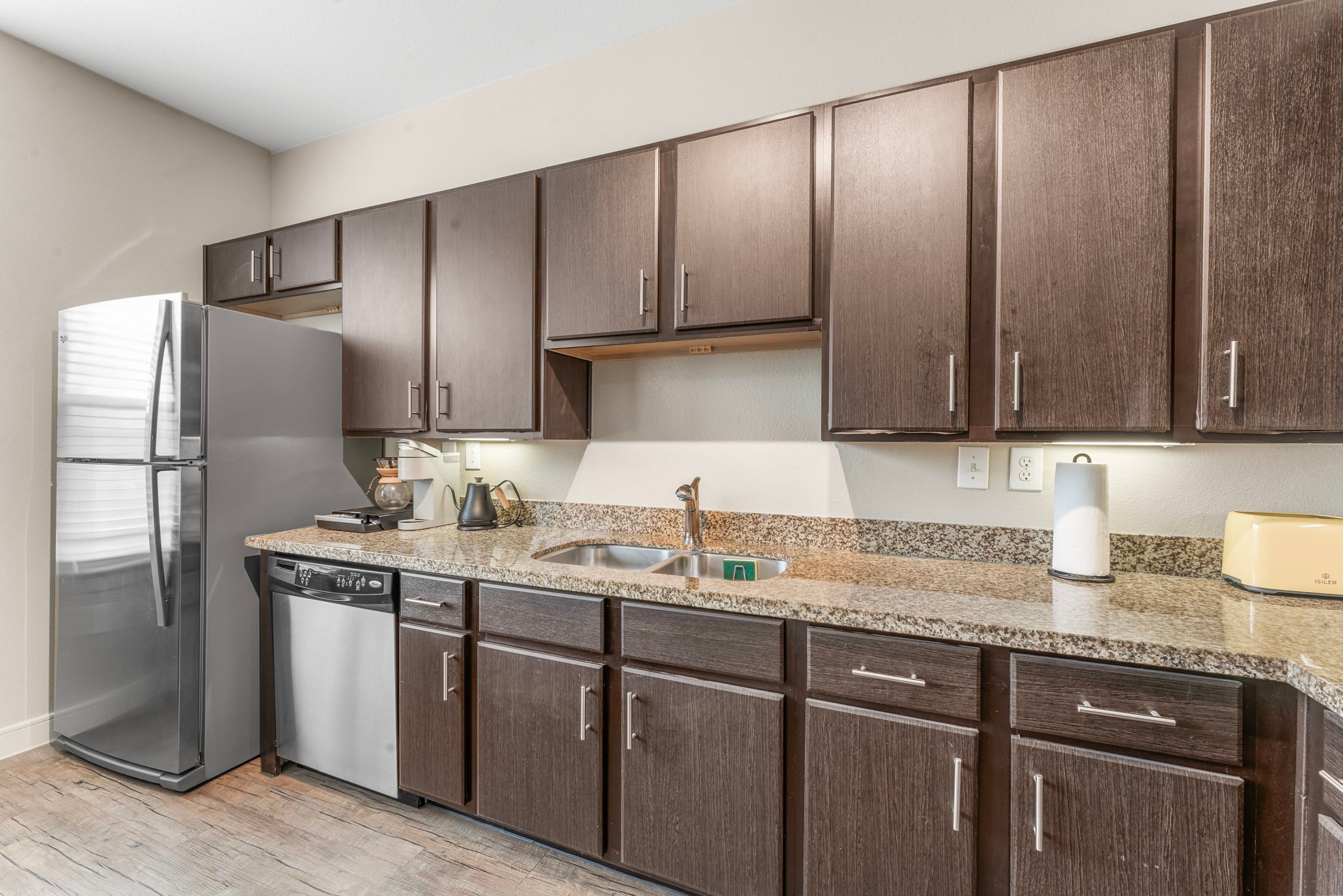 A modern kitchen with dark wooden cabinets, stainless steel appliances, and a granite countertop.