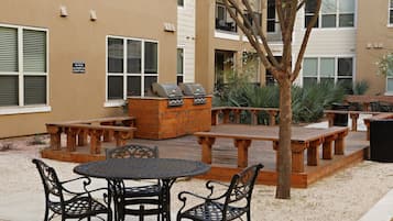 Eine Terrasse im Freien mit einem runden Tisch und Stühlen, einem Grill und Holzbanken.